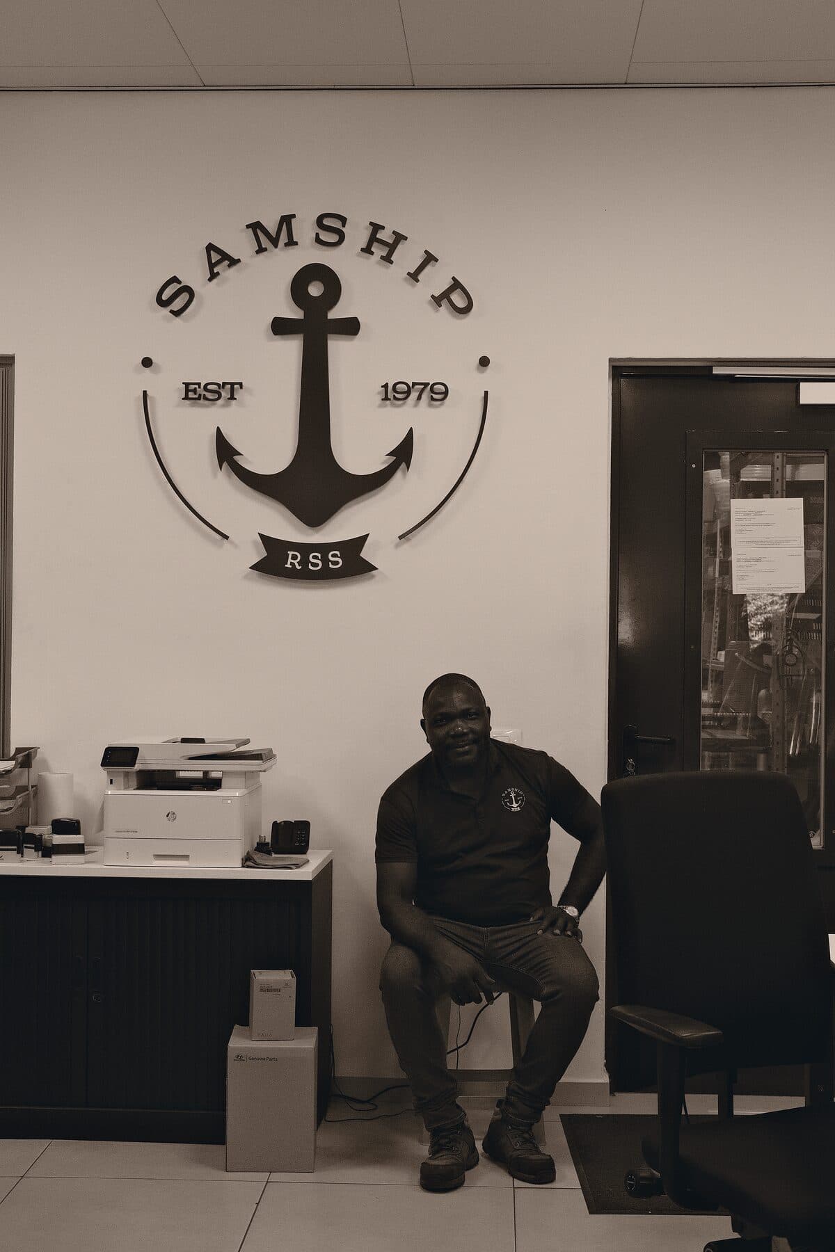 A Samship colleague in the office, beneath the crest painted on the wall